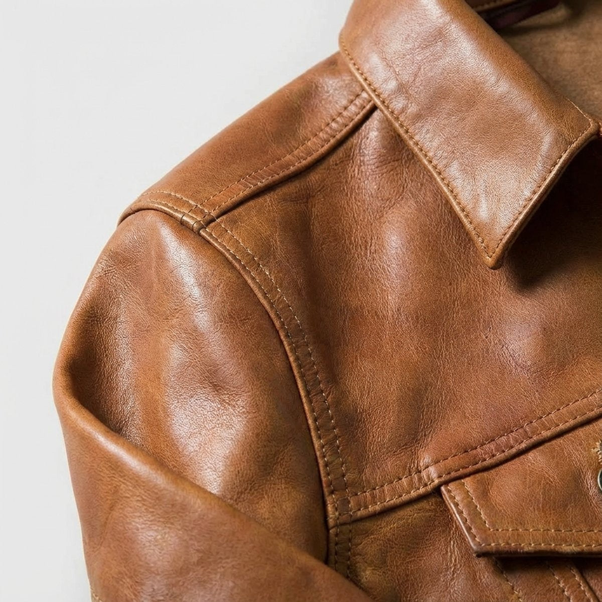 Close-up of tan leather jacket collar and shoulder seam with button placket