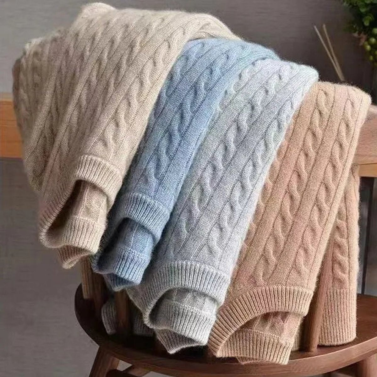 Folded cable knit jumpers in cream, blue, grey and tan draped over chair