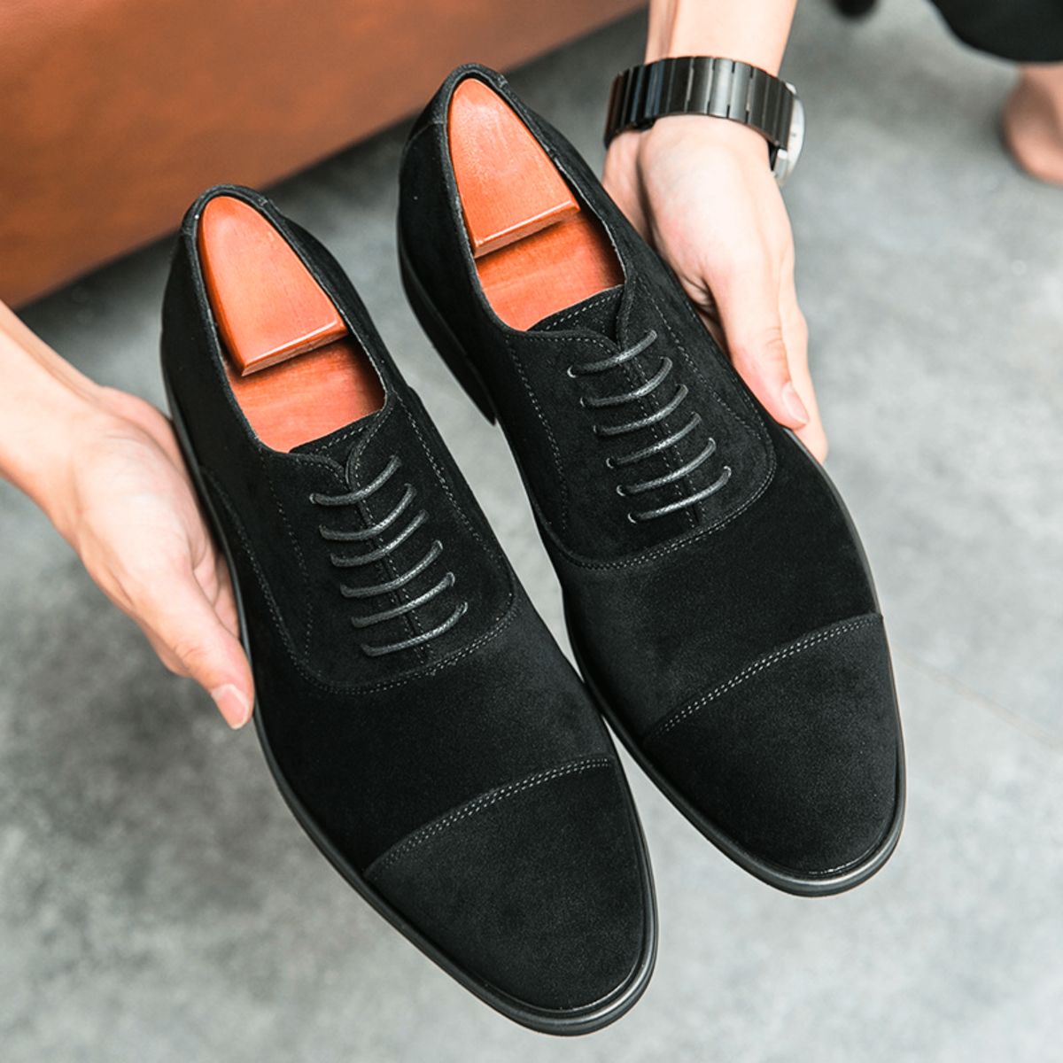 Pair of black suede cap-toe Oxford shoes held in hand