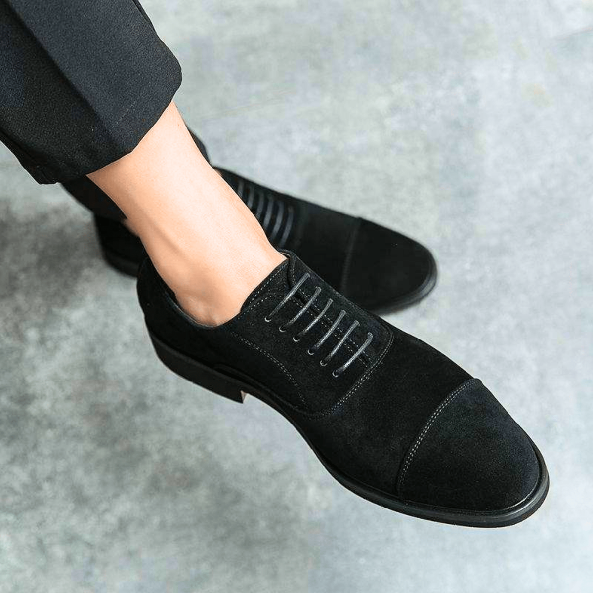 Close-up of black suede cap-toe shoe with lace detailing worn on foot