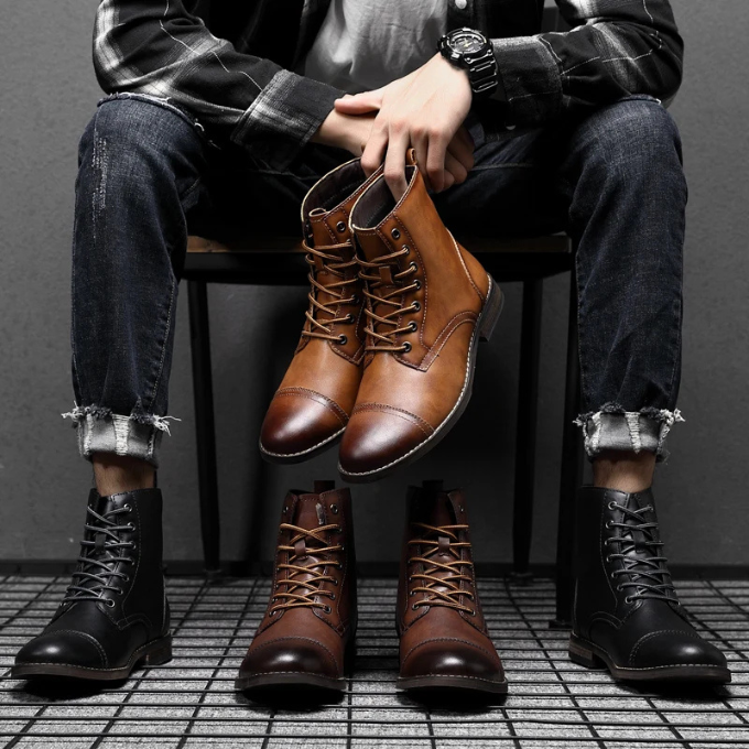 Seated man holding brown leather boots above black and tan pairs on floor