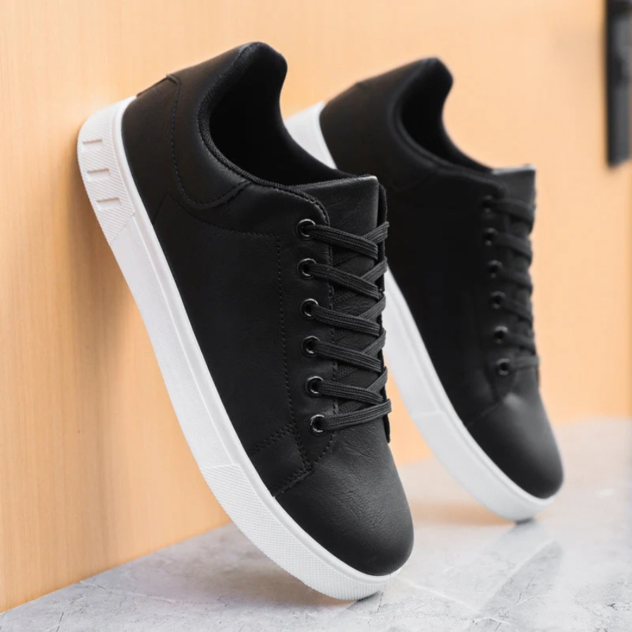 Black leather trainers propped against wall showing white outsoles