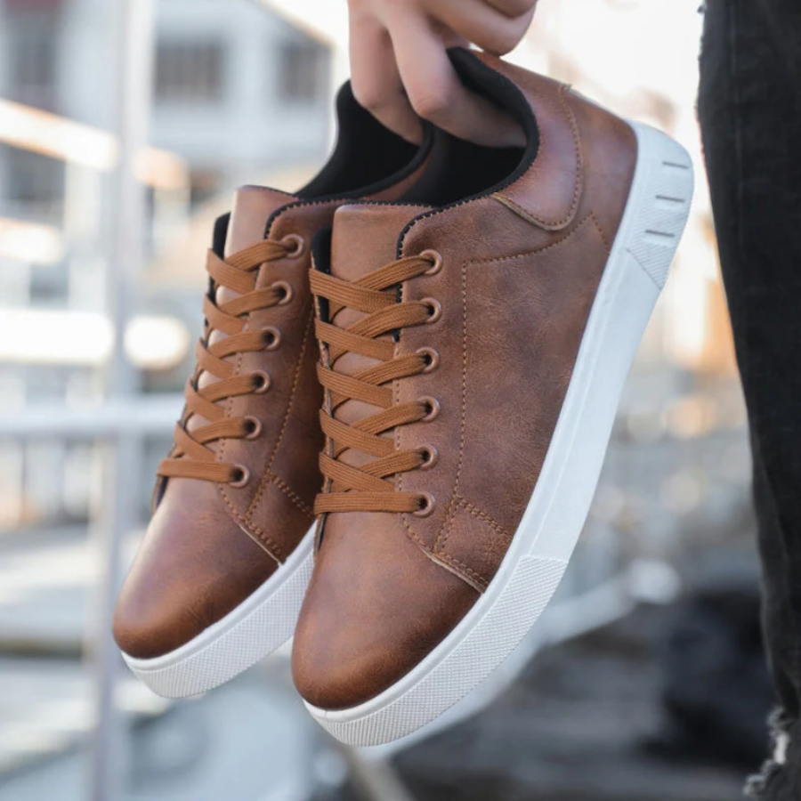Tan leather trainers dangling from hand, showcasing white platform soles