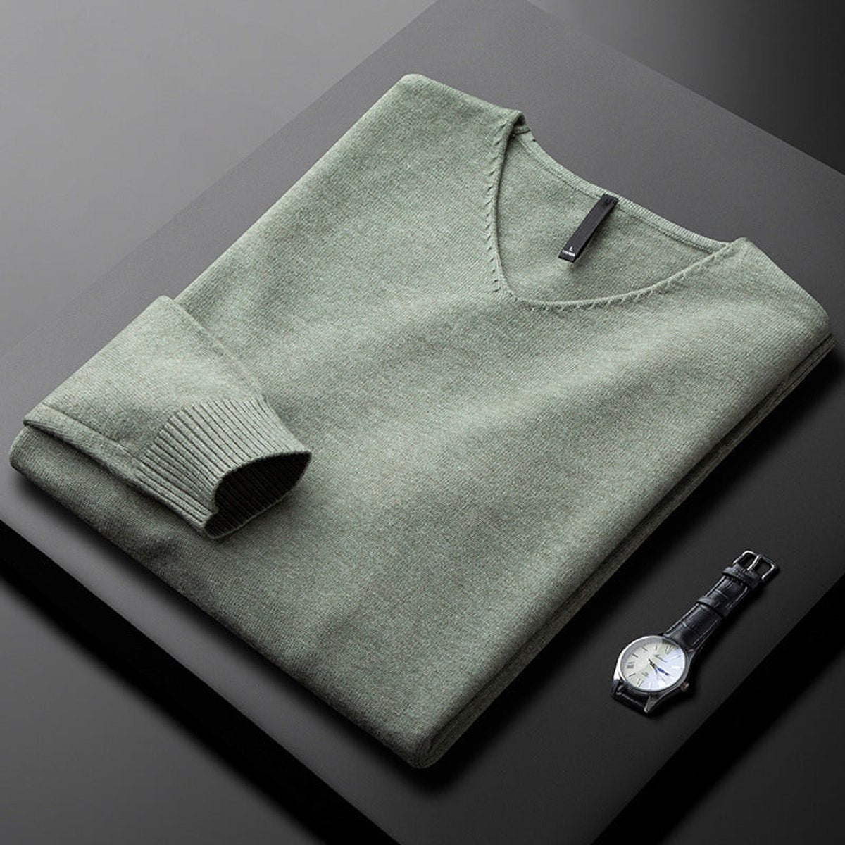 Folded sage green V-neck jumper with ribbed cuffs beside a leather watch