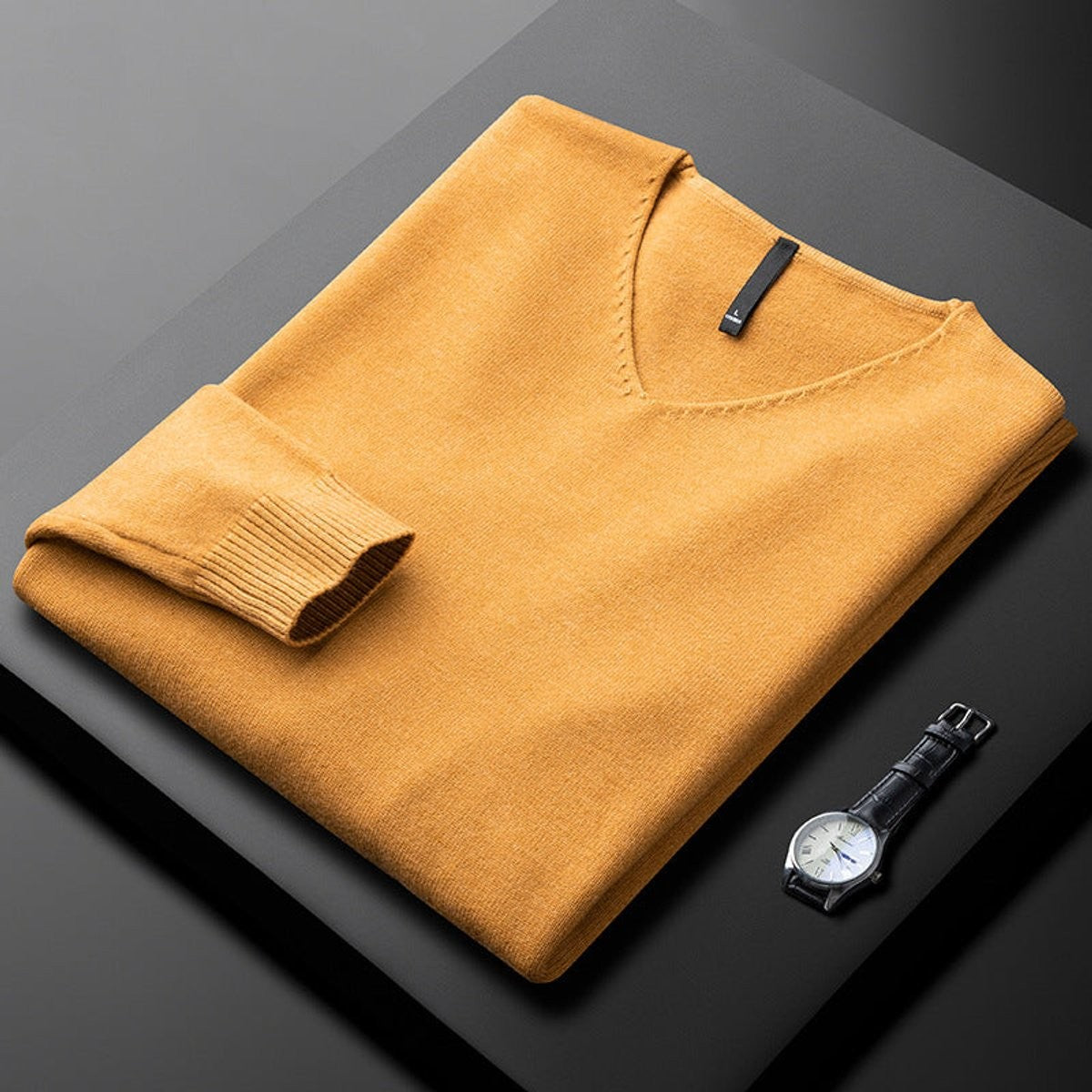 Folded mustard yellow V-neck jumper with ribbed cuffs beside a leather watch