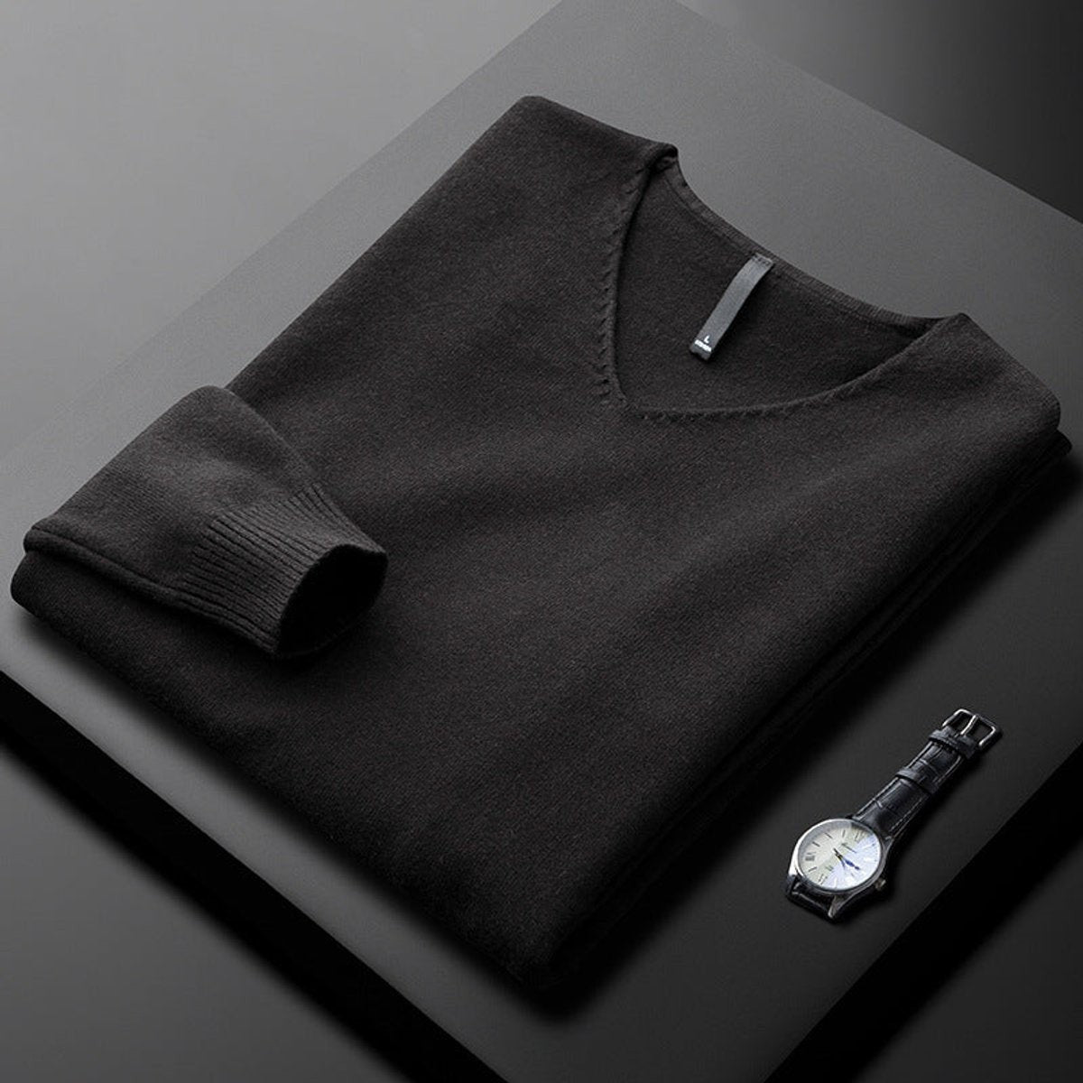 Folded black V-neck jumper with ribbed cuffs beside a leather watch
