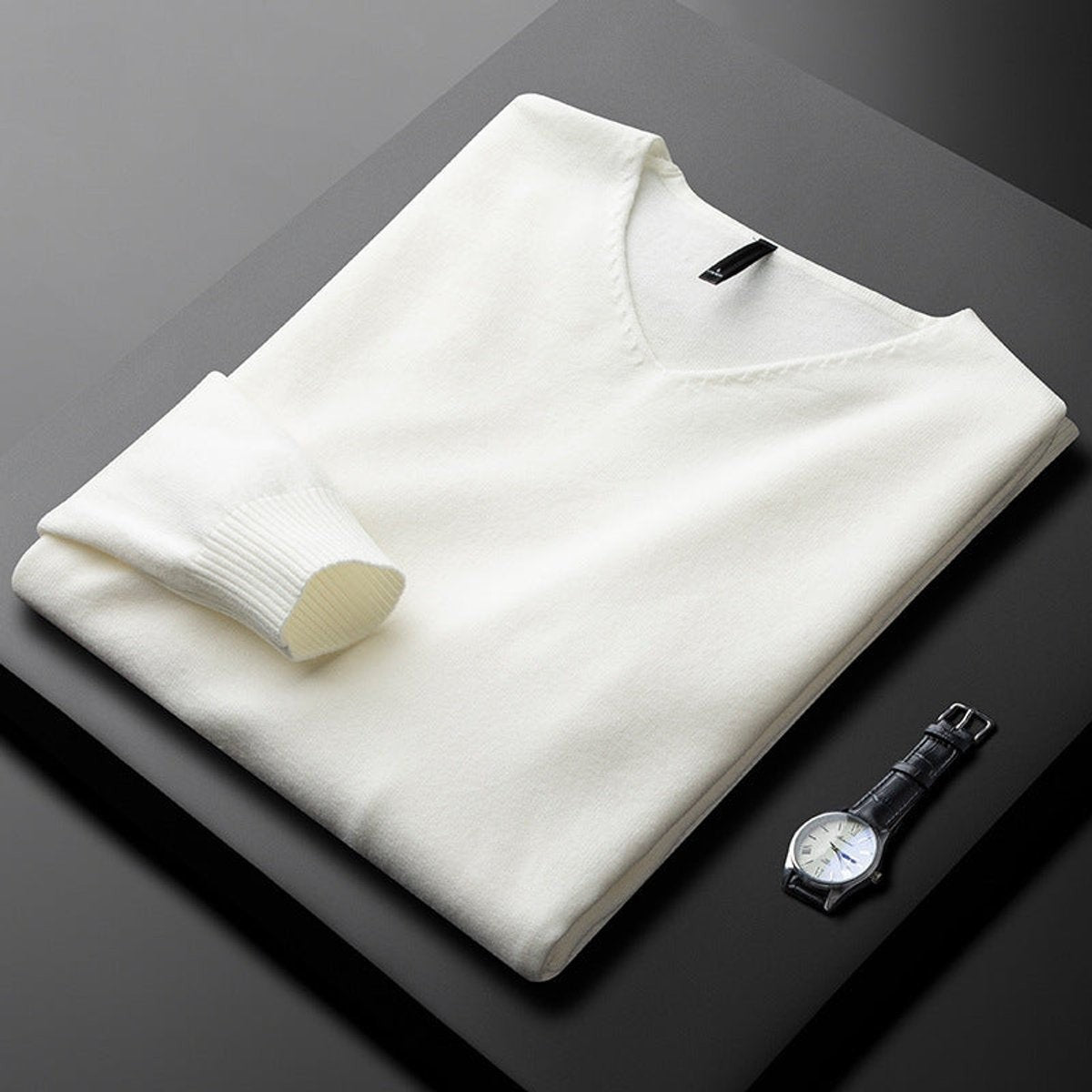 Folded ivory white V-neck jumper with ribbed cuffs beside a leather watch