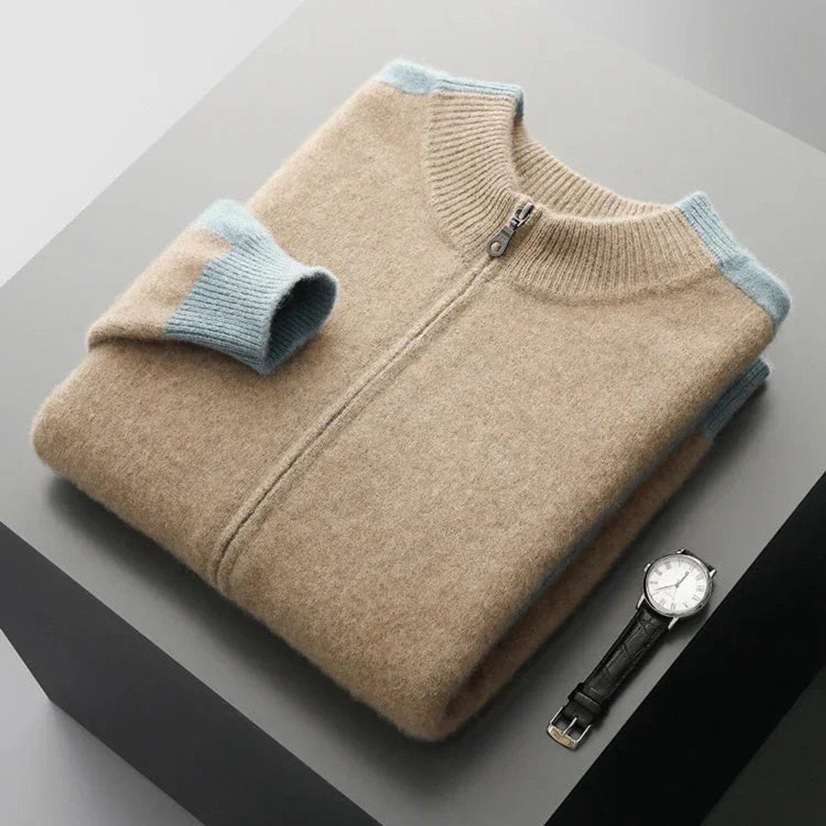 Pale blue cashmere zip cardigan folded flat next to a leather strap watch