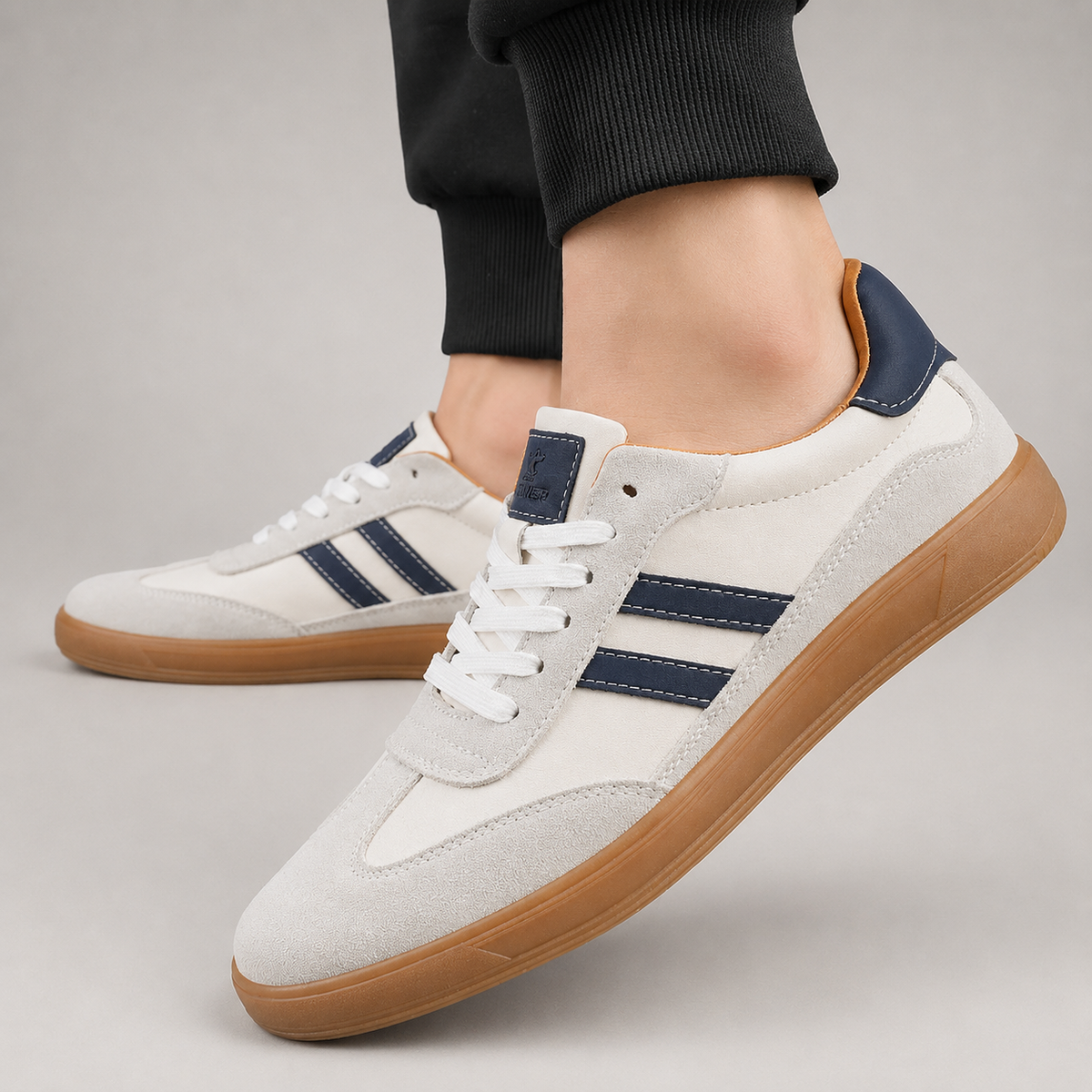 Close-up of white suede trainer with navy stripes worn on foot