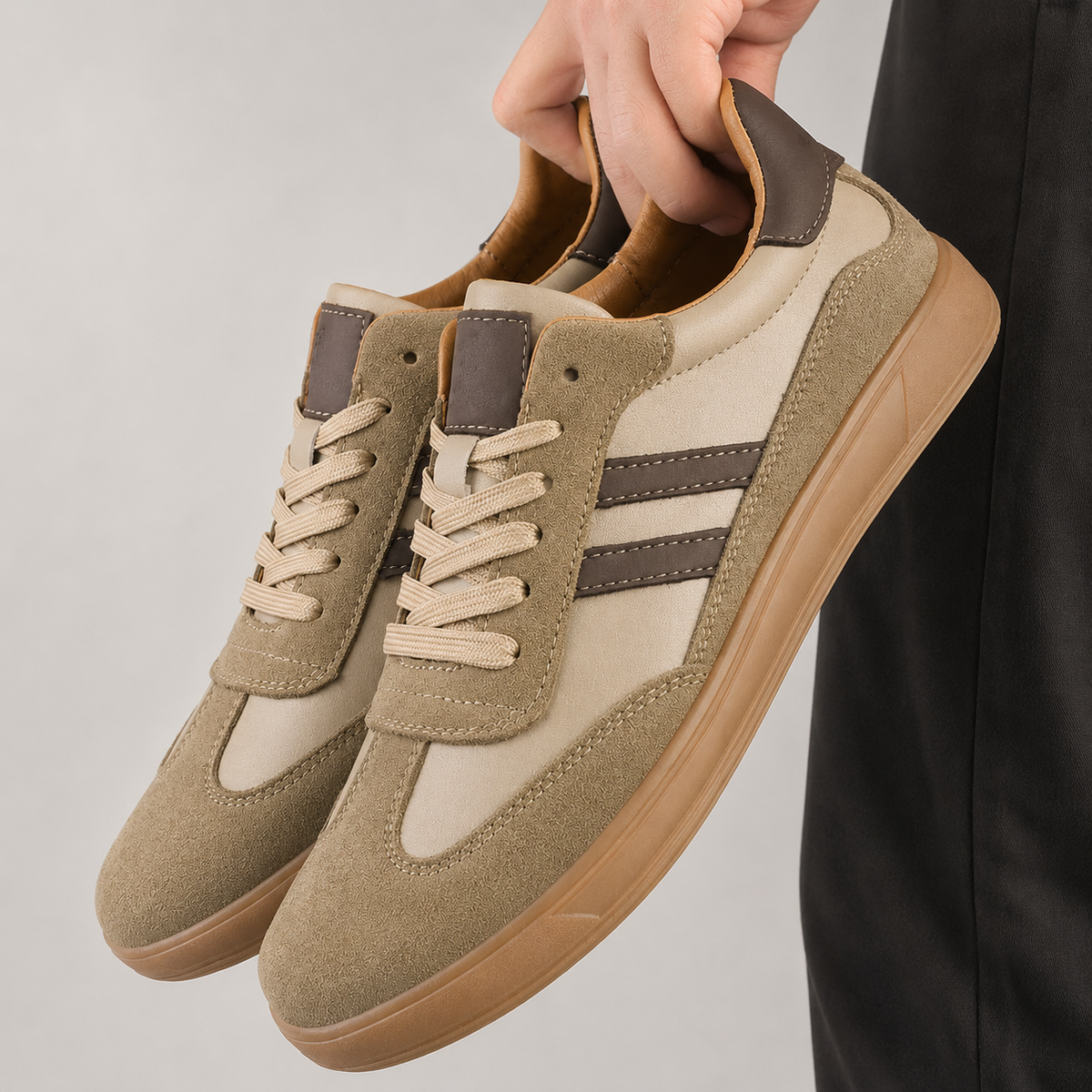 Hand holding pair of beige suede trainers with brown stripes