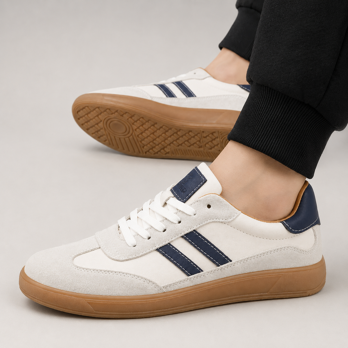 Man wearing white suede trainers with navy stripes and gum soles