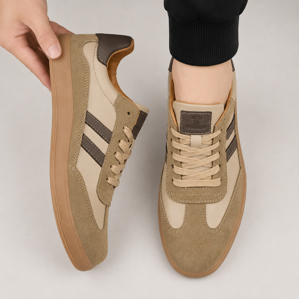 Beige suede trainers with brown stripes held up by hand