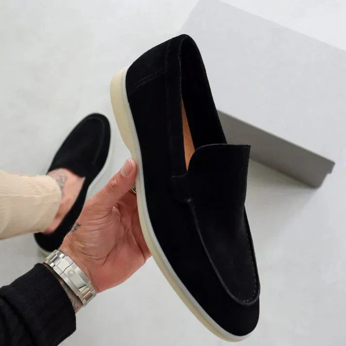 Hand holding black suede loafer beside matching shoebox