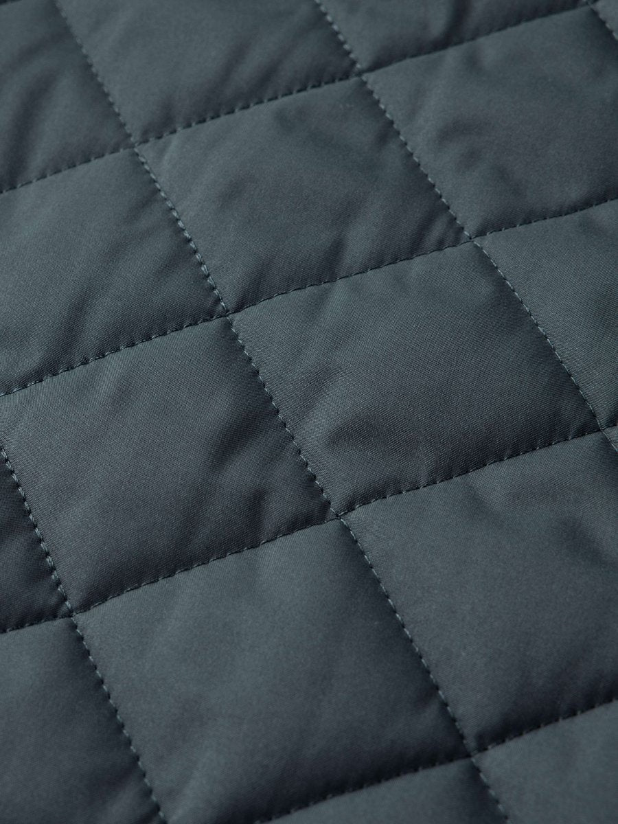 Detail shot of dark teal diamond-quilted fabric texture on bomber jacket