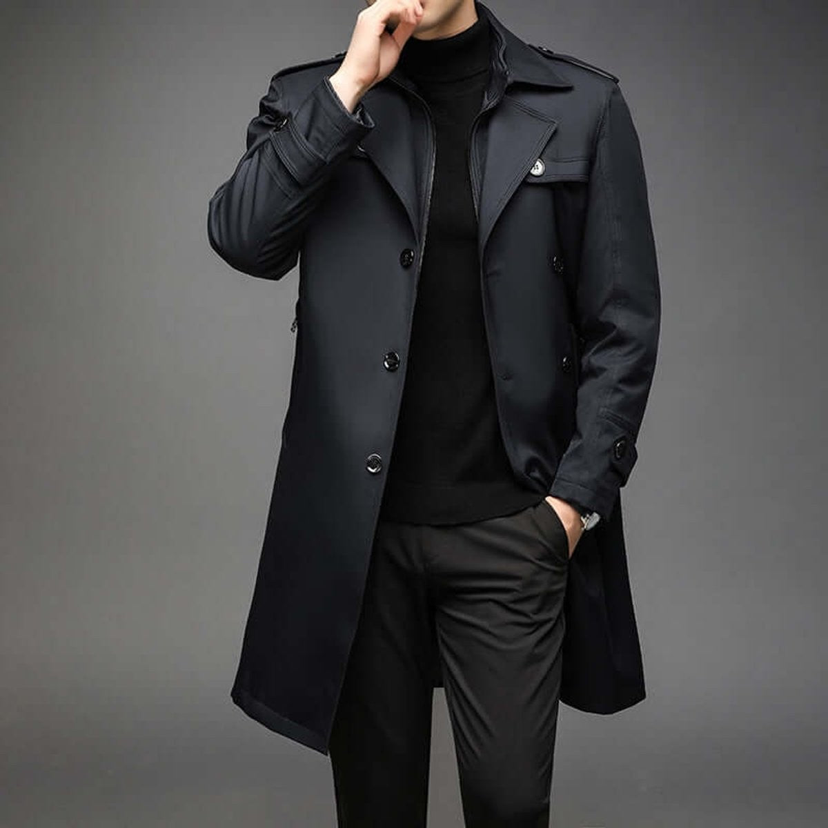Man adjusting collar of long black trench coat with double-breasted buttons