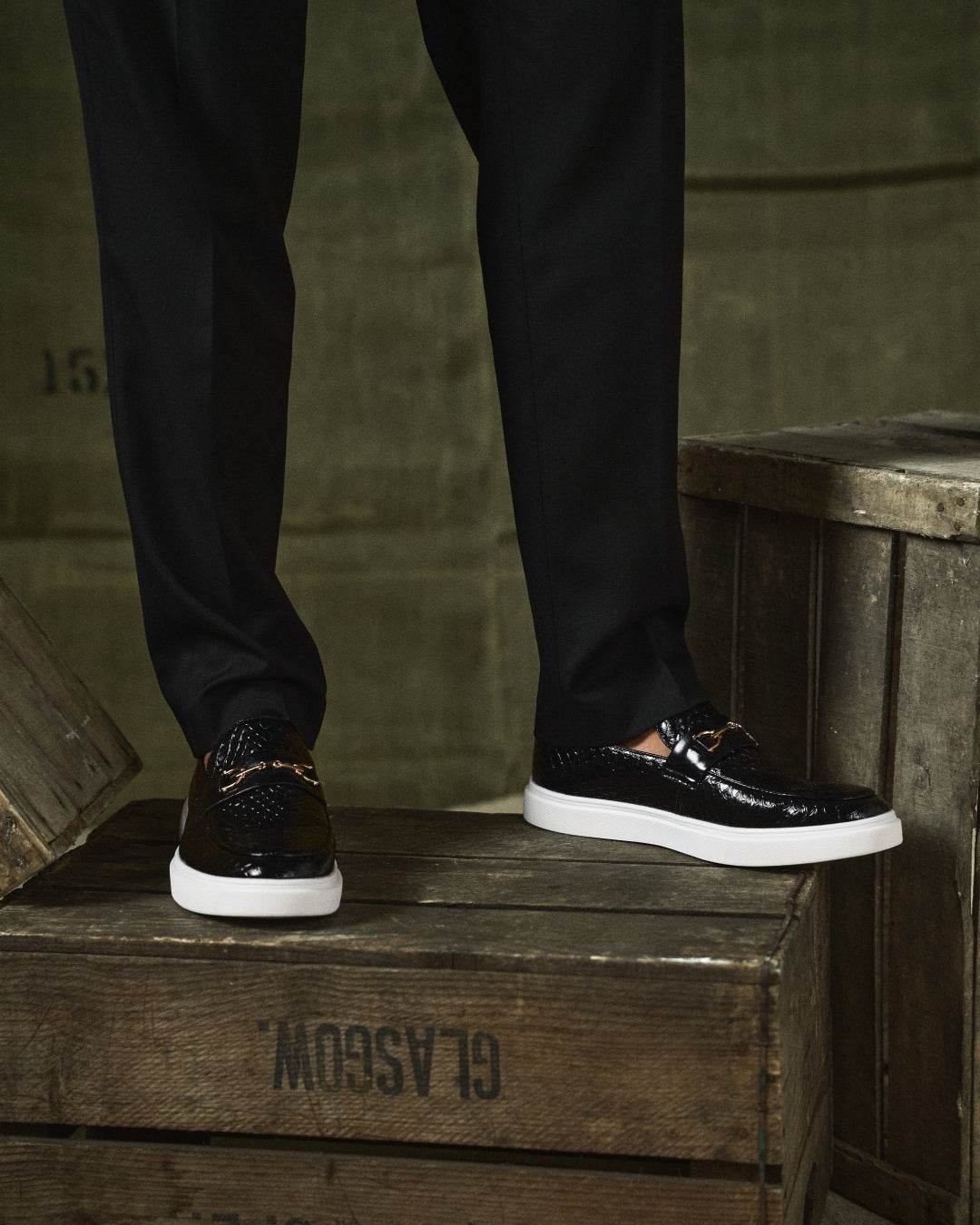 Close-up of black embossed leather loafers worn with tailored black trousers