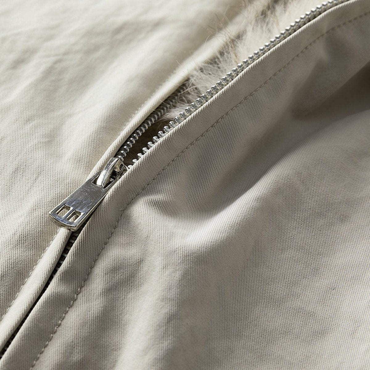 Close-up of silver zip pull against cream bomber jacket fabric