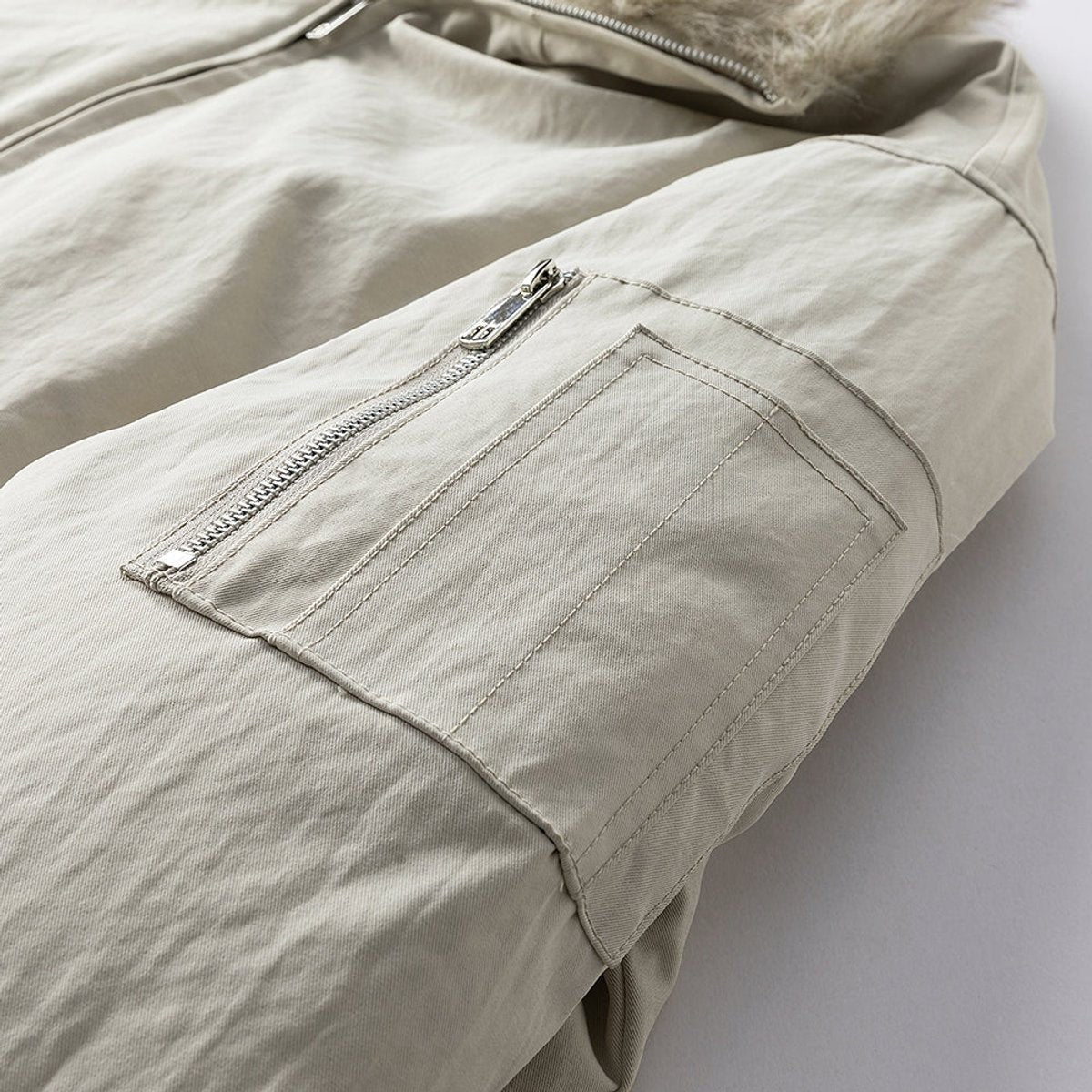 Close-up of zip sleeve pocket on cream wind-resistant bomber jacket