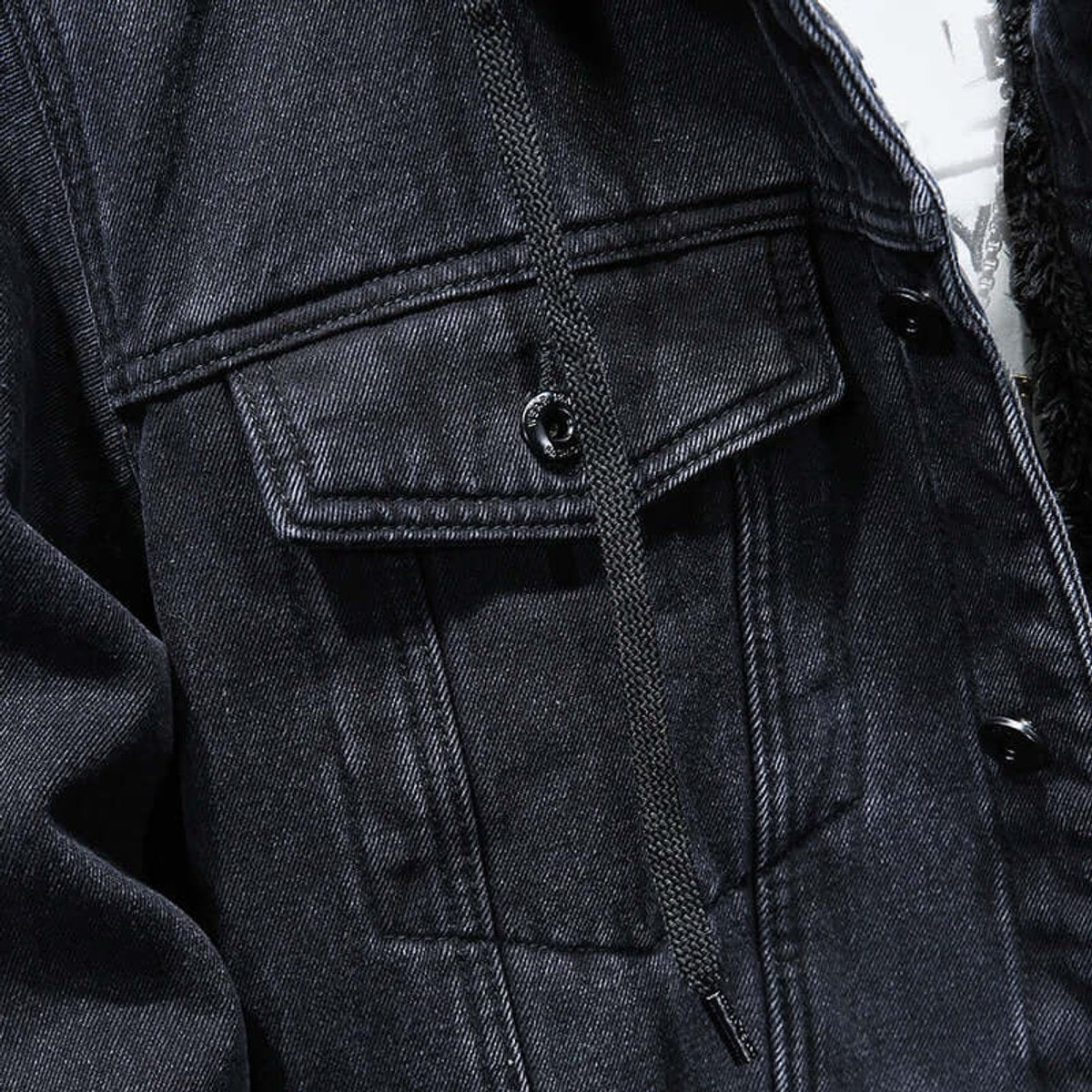 Detail of chest pocket and drawstring cord on black denim jacket