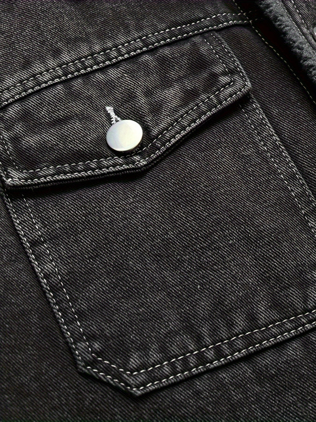 Close-up of black denim jacket pocket flap with press-stud button