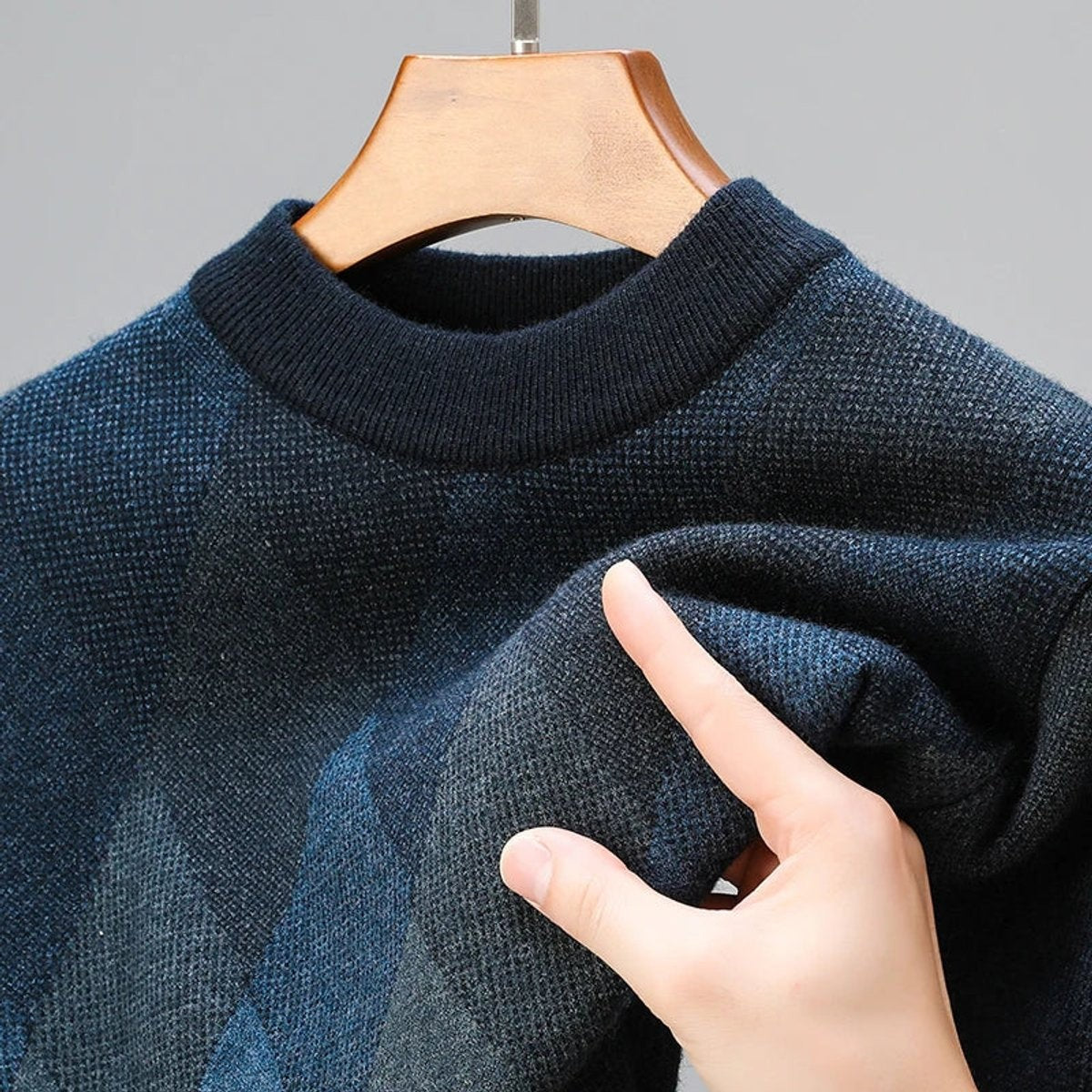 Detail shot of blue argyle pullover fabric being gently pinched