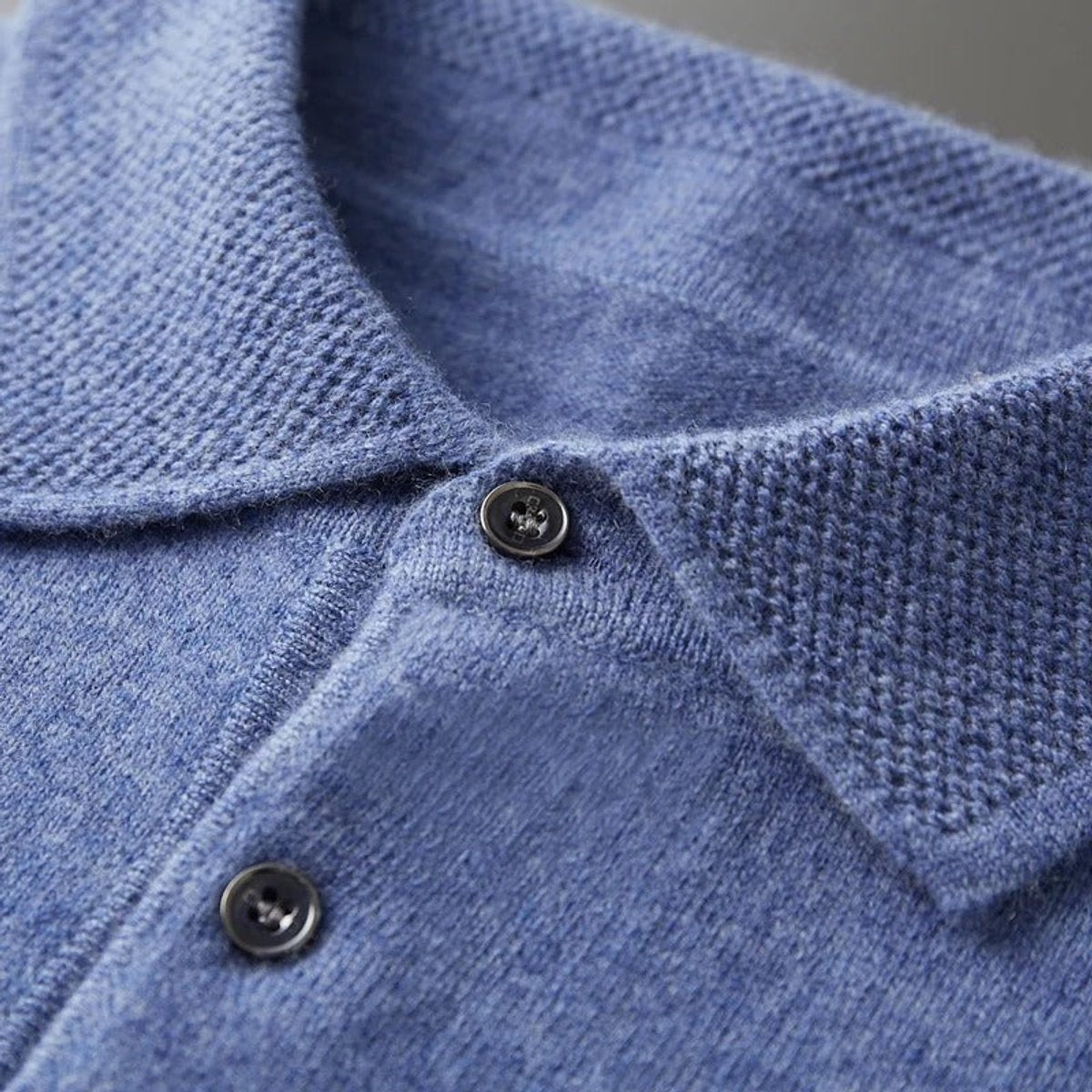 Close-up of blue knitted polo collar showing button and ribbed texture