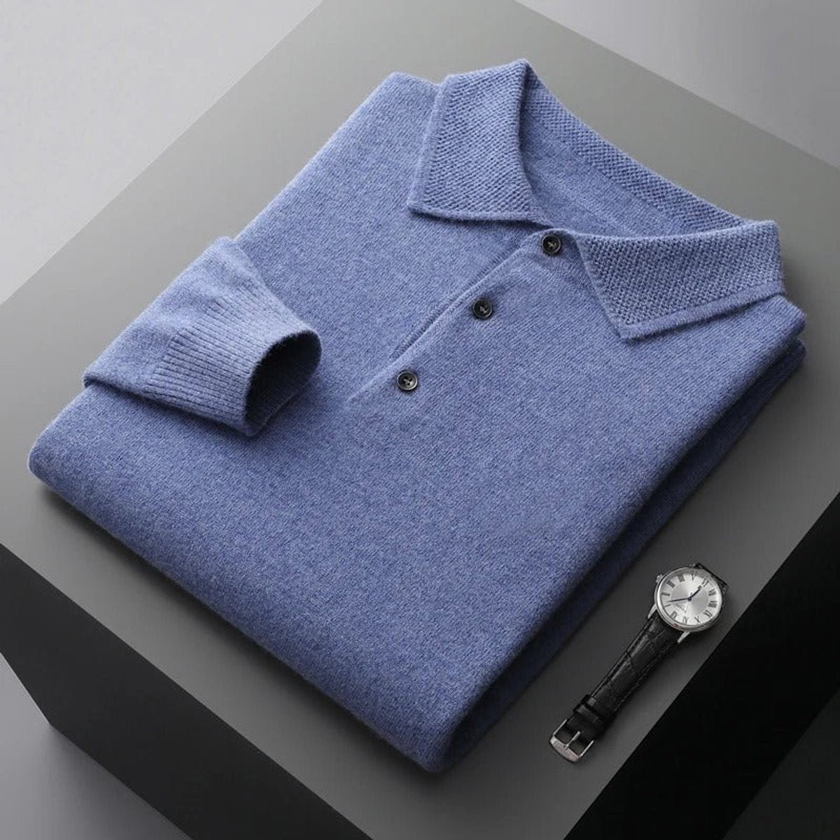 Folded blue cashmere polo jumper displayed beside a wristwatch
