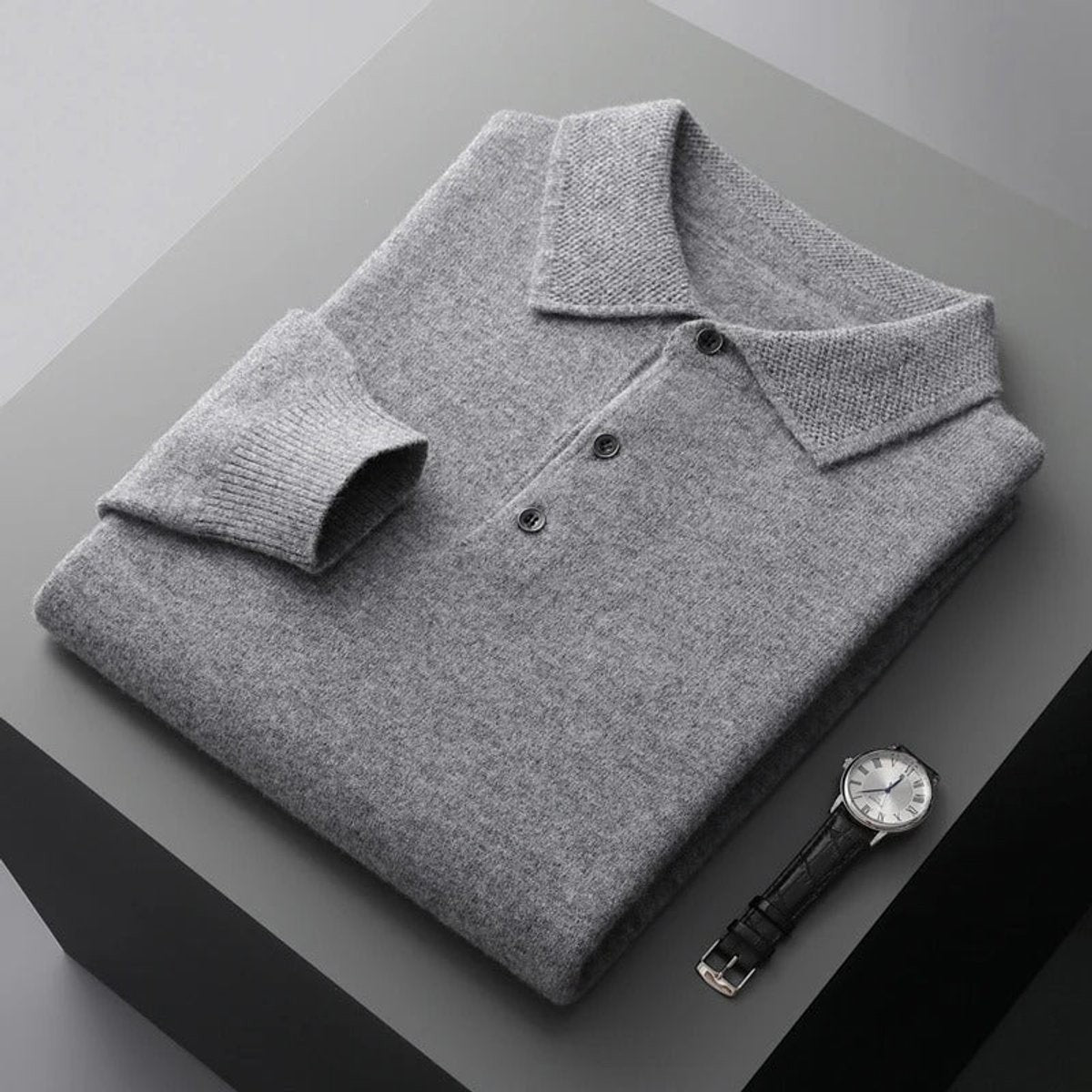 Grey cashmere knitted polo jumper folded beside a leather watch
