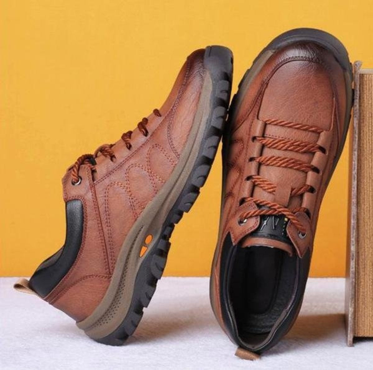 Brown and black leather lace-up shoes paired together against yellow backdrop