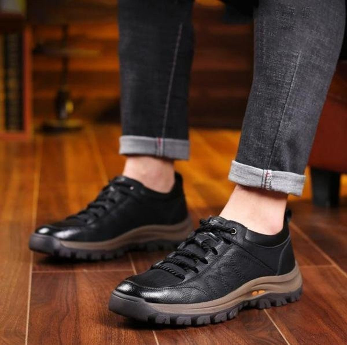 Man seated wearing black leather lace-up casual shoes on wooden floor