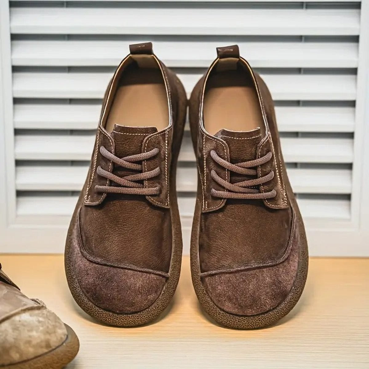 Dark brown leather shoes with suede toe held by both hands