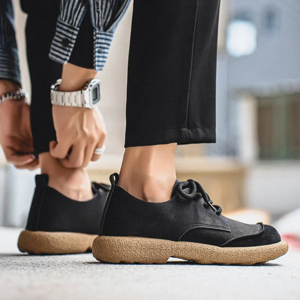 Black leather trainers worn with black trousers on concrete floor
