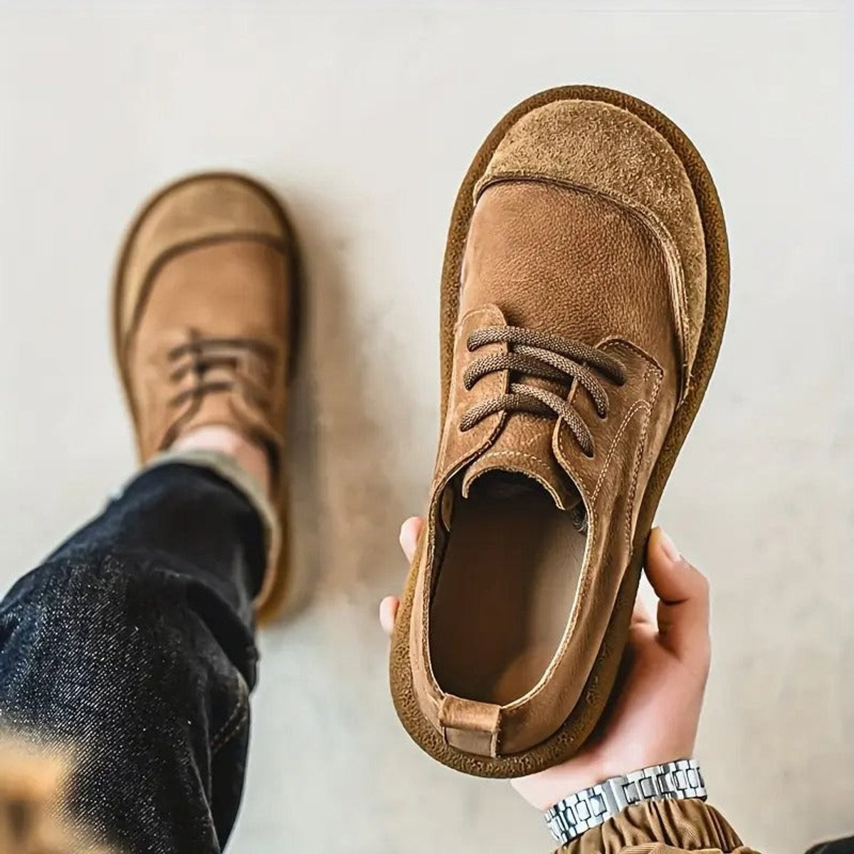 Camel leather lace-up shoe held aloft showing cushioned insole