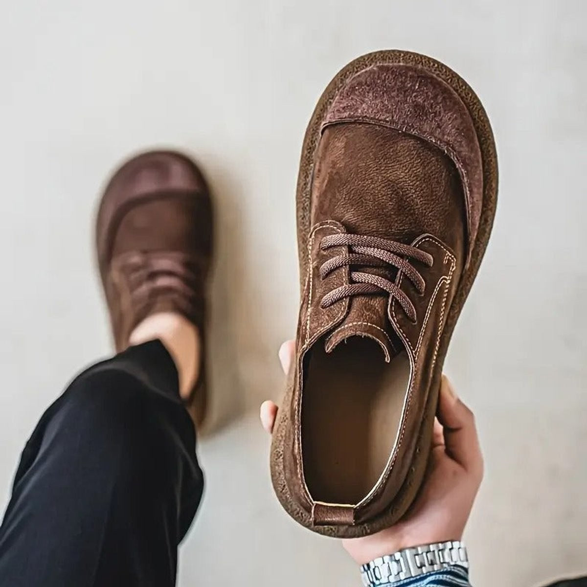 Dark brown leather shoe held up displaying soft suede toe cap