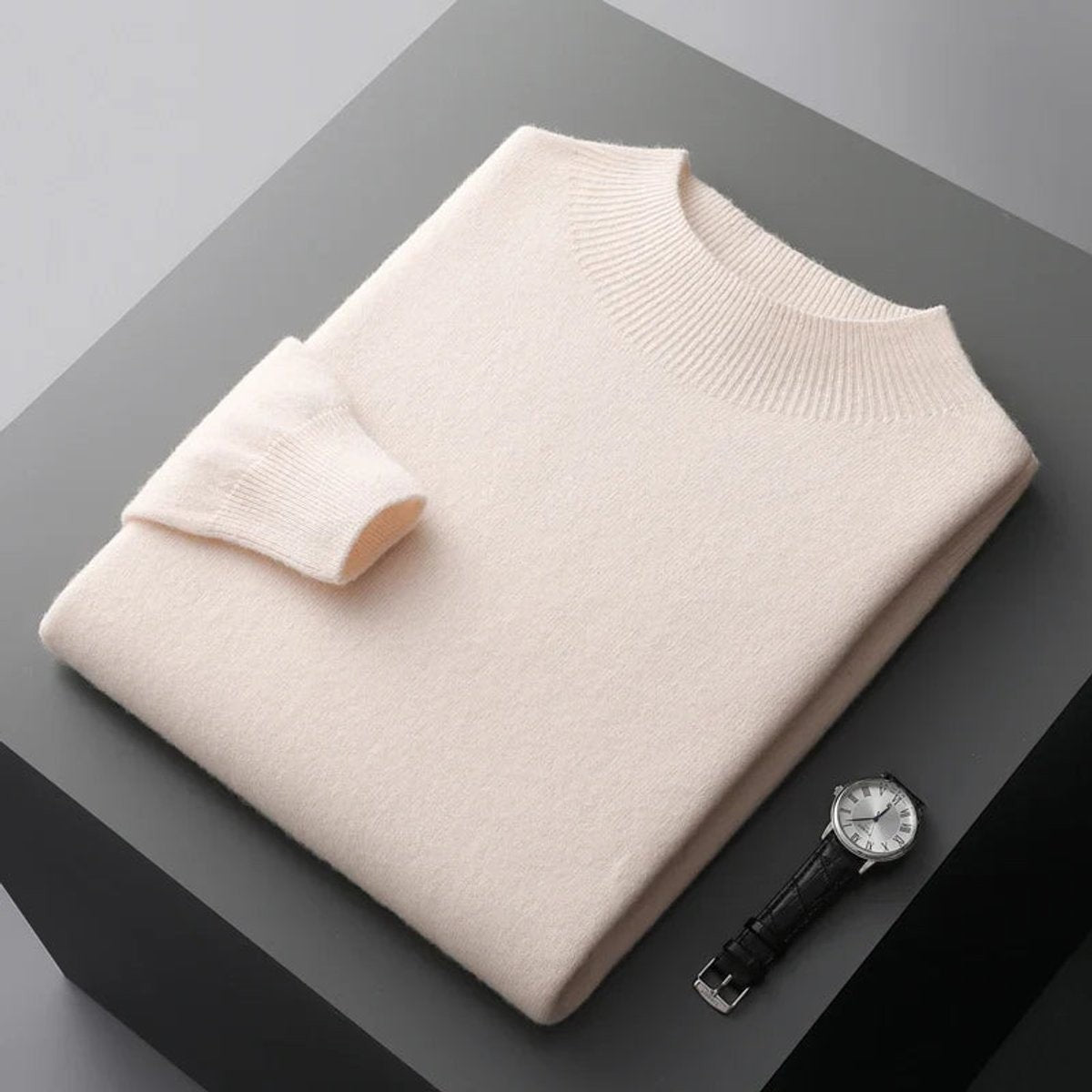 Cream half-neck knitted jumper folded on display next to a classic wristwatch