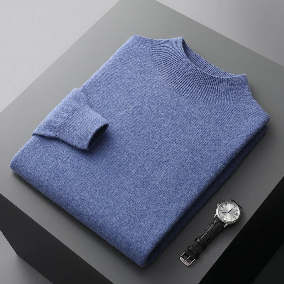 Denim blue half-neck jumper folded neatly alongside a leather-strap watch