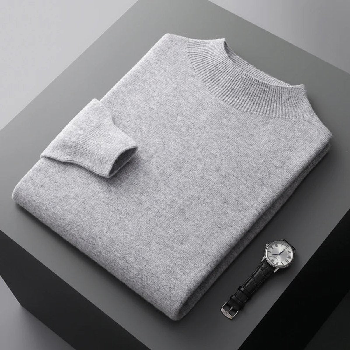 Light grey cashmere blend jumper folded with ribbed mock neck beside a wristwatch