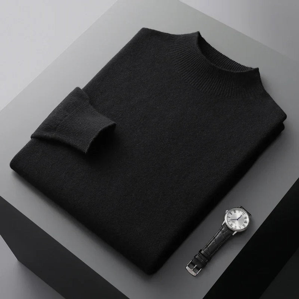Black half-neck knitted jumper folded neatly next to a leather-strap watch