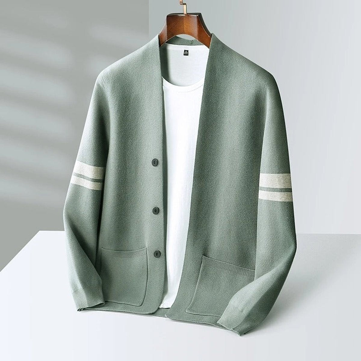 Sage green button-up cardigan with cream stripes, displayed on wooden hanger