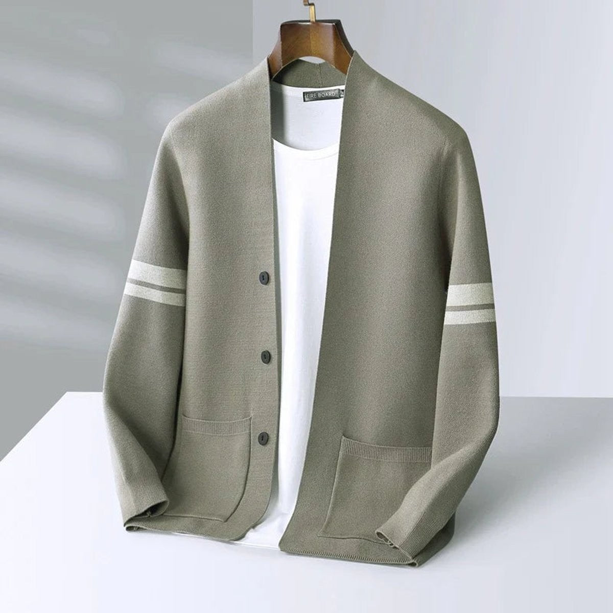 Olive green cardigan with cream sleeve stripes hung against grey backdrop