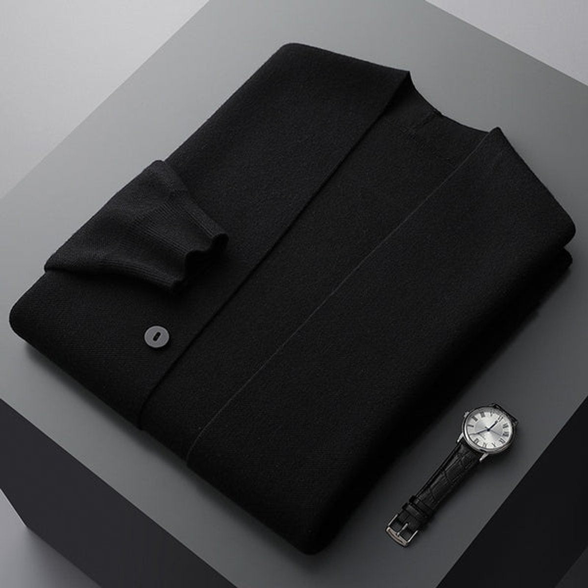 Folded black knitted cardigan styled beside a classic leather wristwatch