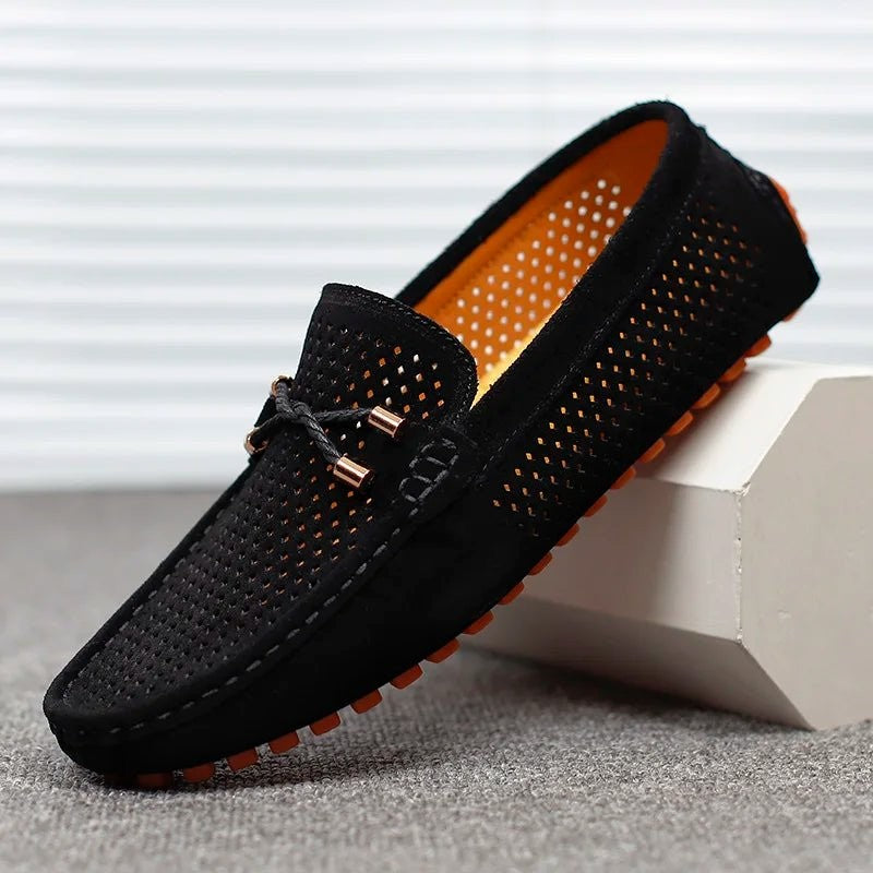 Black suede perforated driving loafers propped against a white block
