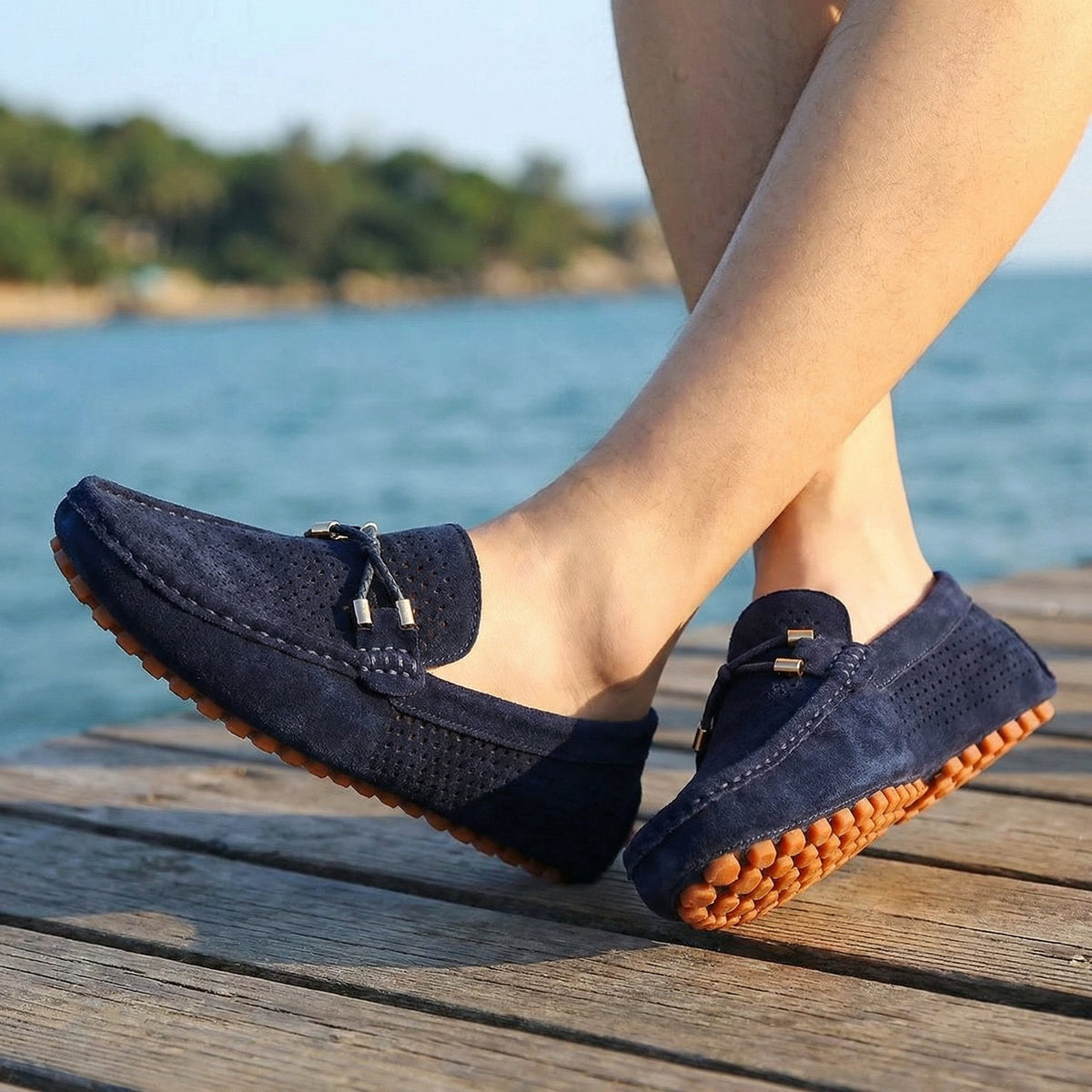 Man wearing navy perforated suede loafers on a wooden pier by the sea