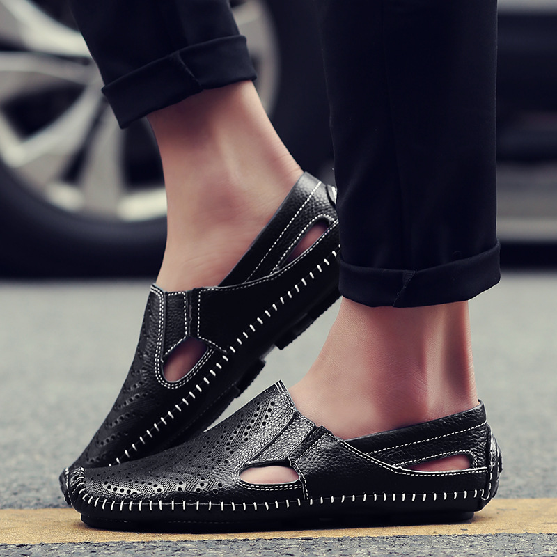 Black perforated leather sandals worn on foot near a car tyre kerb