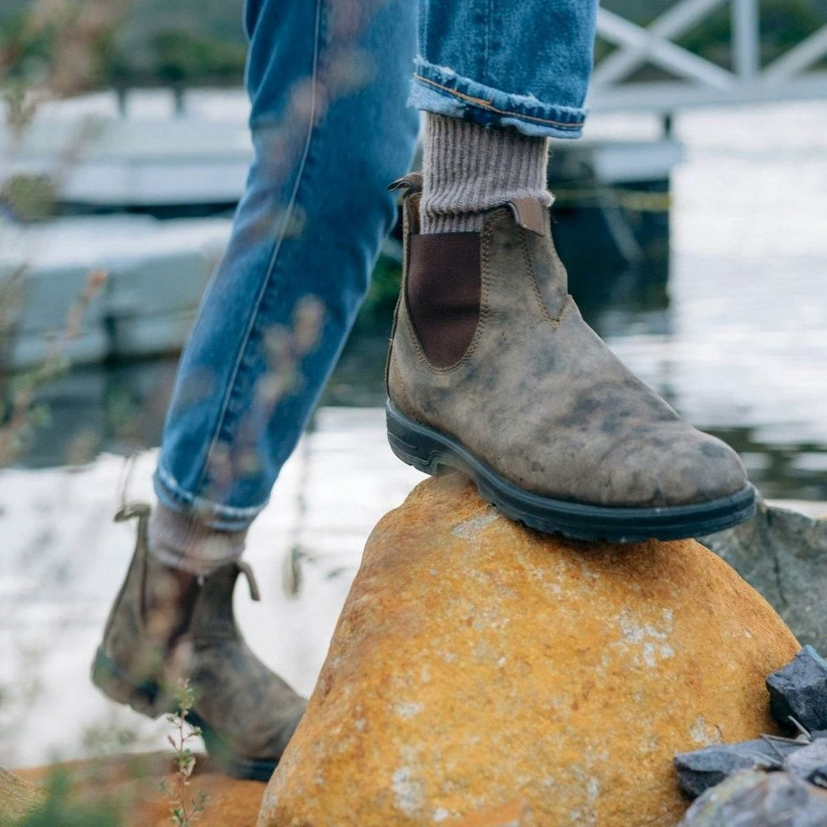 Rustic brown leather Chelsea boots worn outdoors on a rock by the water