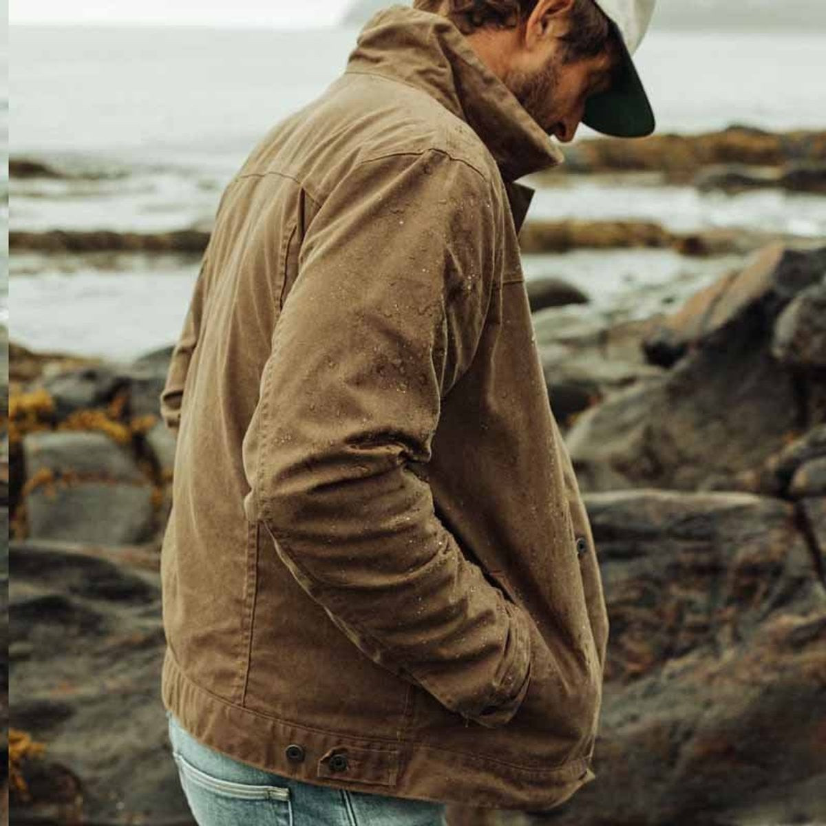 Side view of rugged brown utility jacket worn near rocky shoreline
