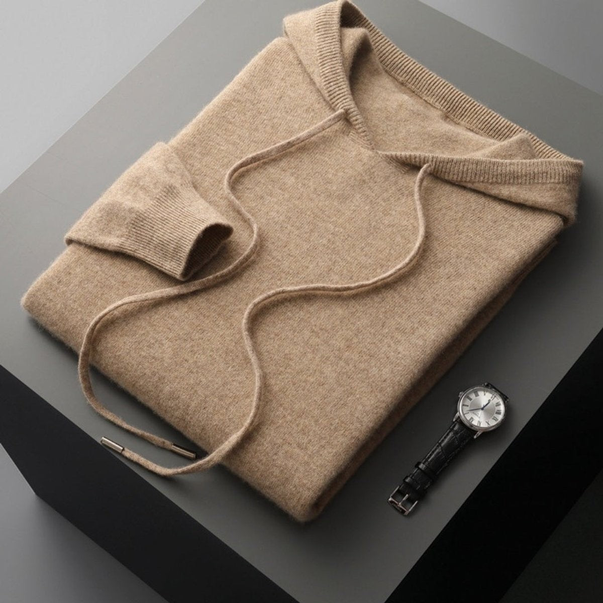 Folded beige knitted hoodie jumper with drawstring beside a leather watch