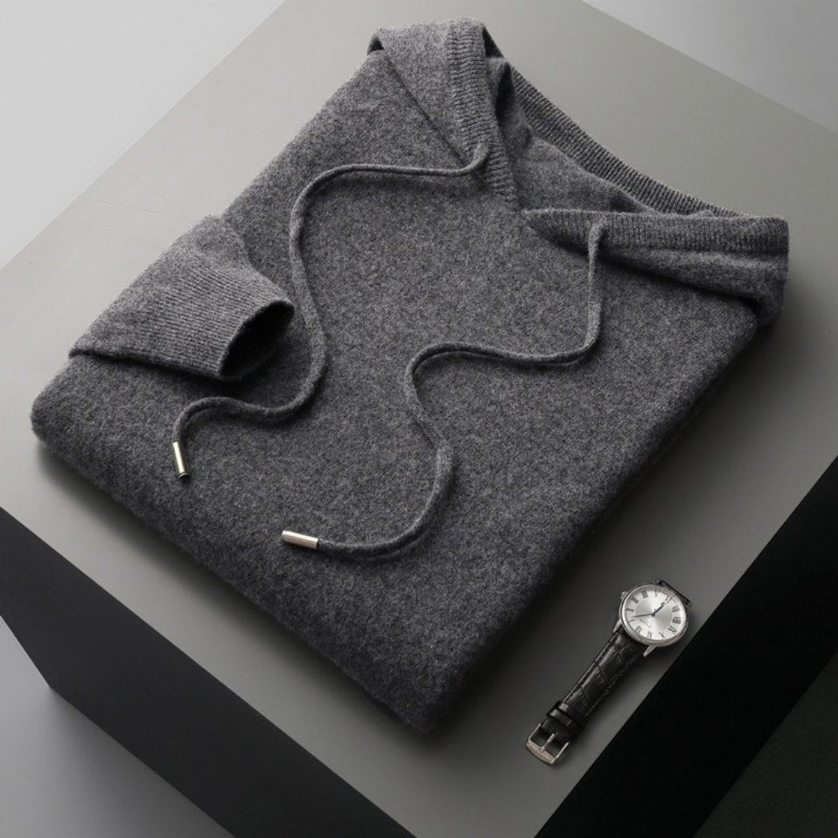 Folded charcoal grey knitted hoodie jumper with drawstring on grey surface