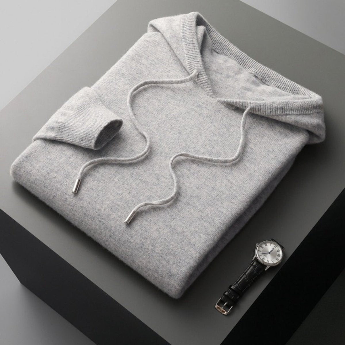 Folded light grey cashmere hoodie jumper with drawstring beside a wristwatch