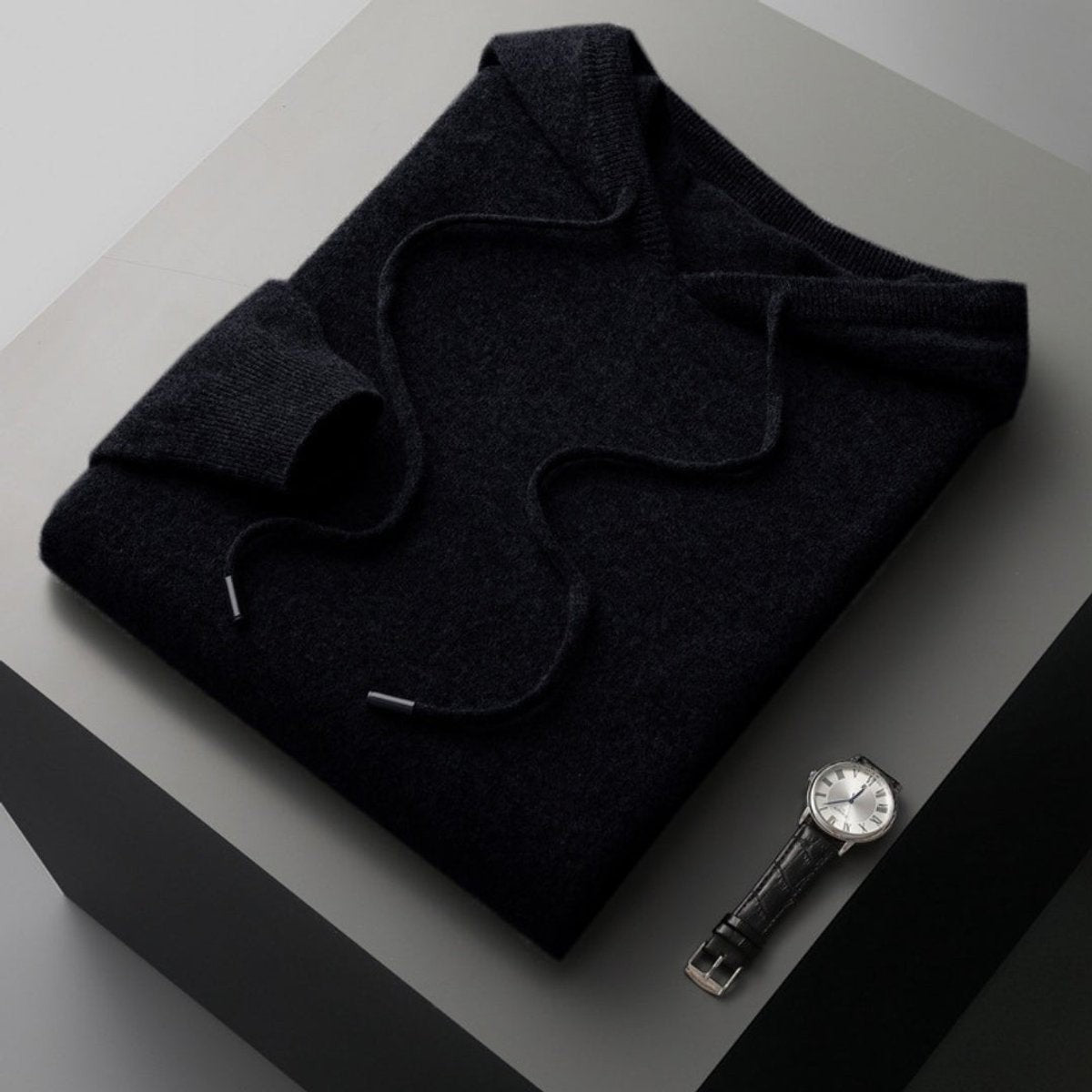 Folded black knitted hoodie jumper with drawstring hood on dark surface